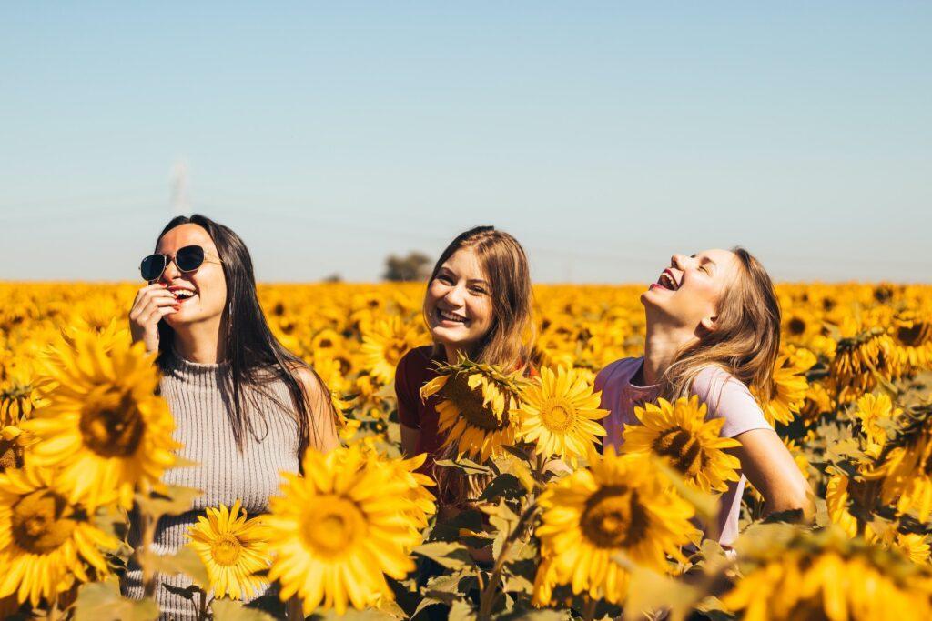 Three teen girls laughing in a sunflower field, symbolizing joy, friendship, and the power of confidence building activities for teenagers.

